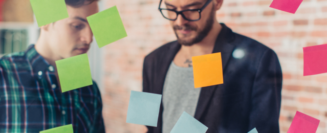Two professionals planning a social media strategy with sticky notes on a glass board